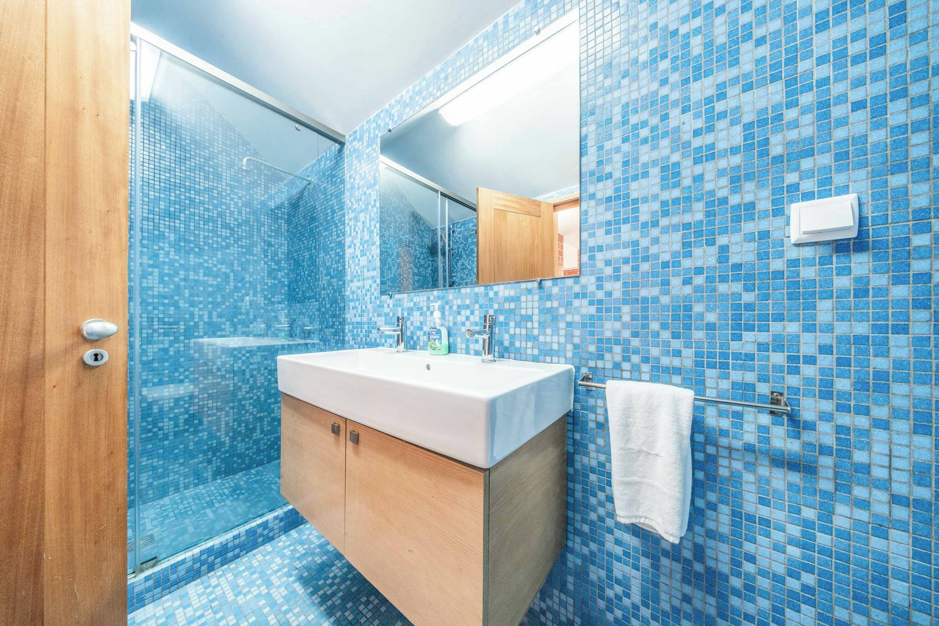 A bathroom with a tiled shower, a sink, and a mirror.
