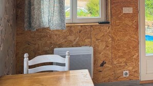 Een kamer met een houten plafond, een raam met uitzicht op groen, een witte stoel en een klok aan de muur.