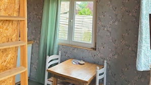 Een rustieke kamer met een houten plafond, een wandklok, een televisie, een raam met uitzicht en een tafel met stoelen.