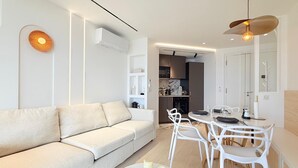 En moderne stue med sofa, spisebord, stole, en klimaanlæg og et køkkenområde.