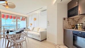 Et moderne køkken med indbygget ovn og mikroovn, et spiseområde med et hvidt bord og stole, samt en sofa i opholdsstuen.