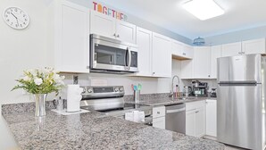 A modern kitchen with white cabinets, stainless steel appliances, a granite countertop, and a clock on the wall. - Beautiful Condo near Downtown with POOL (Cape Coral)