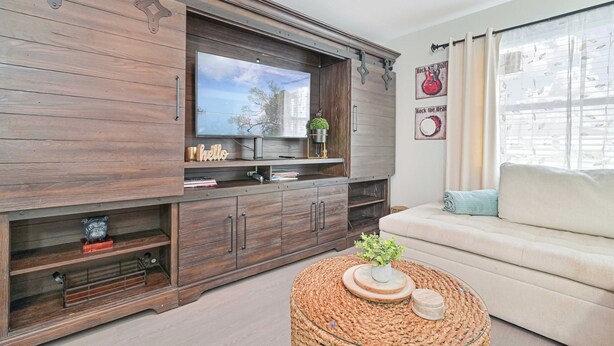 A living room with a TV, wooden cabinet, sofa, and a round coffee table. - Beautiful Condo near Downtown with POOL (Cape Coral)