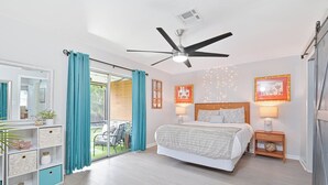 A bedroom with a bed, ceiling fan, bedside lamps, a nightstand, a dresser, and a sliding glass door to a balcony. - Beautiful Condo near Downtown with POOL (Cape Coral)