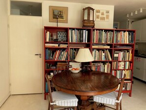 Una mesa de comedor redonda de madera con sillas a rayas, rodeada por una amplia estantería roja llena de libros.