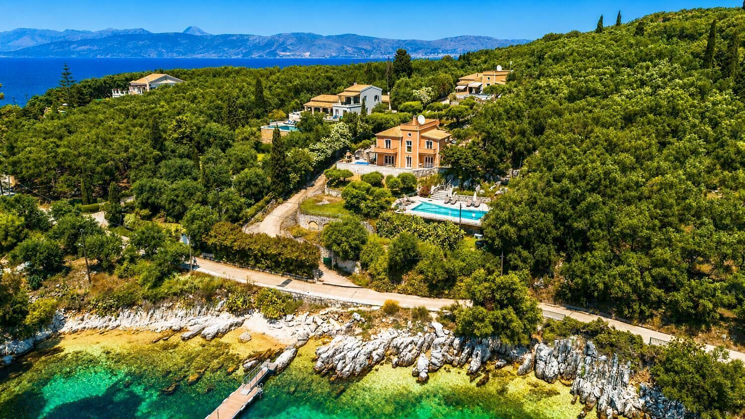 An aerial view of a coastal property with multiple houses, a swimming pool, and a rocky shoreline.
