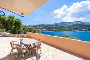 Une terrasse avec une table et des chaises, offrant une vue sur un plan d’eau et un village perché sur une colline.