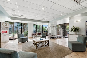 Eine großzügige Lobby mit modernem Design, inklusive einer Sitzecke, einem Couchtisch und einem großen Fenster mit Blick auf Palmen.