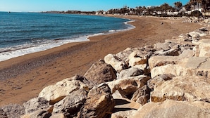 A beach with large rocks in the foreground, a clear blue sky, and a calm sea. - Penthouse in Puerto Banús (Marbella)