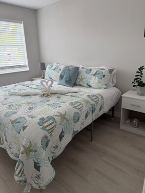 A neatly made bed with a floral quilt, a bedside lamp, and a small plant on a nightstand. - The Perfect Hideaway Retreat for Your FLKeys Getaway (Marathon)