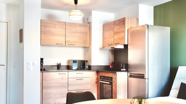 Eine moderne Küche mit Holzausstattung, einem Edelstahlkühlschrank, einer Mikrowelle und einem Esstisch mit Kerze.