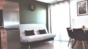 Ein modernes Wohnzimmer mit einer Couch, einem Esstisch mit Stühlen, einem Kühlschrank und einer Wanduhr.