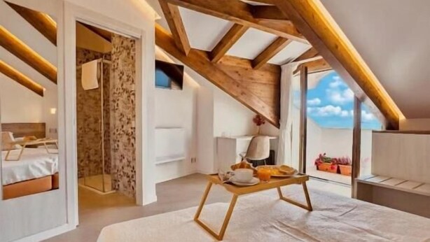 A bedroom with a large bed, wooden beams, a small table, and a view of the sky.