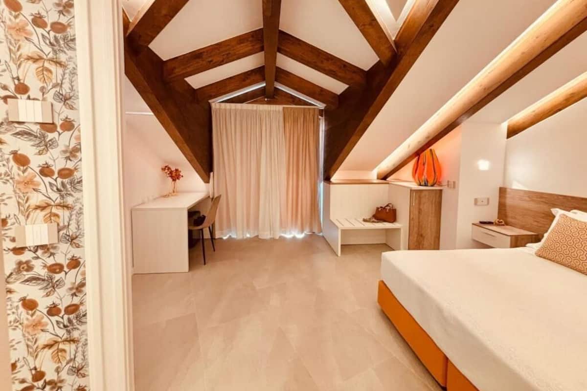 Ein Schlafzimmer mit schrägen Wänden, einem Bett, einem Schreibtisch und einem Stuhl.