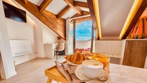 A breakfast setup with croissants, coffee, and a fruit bowl on a wooden table in a room with exposed wooden beams and a view through a window.