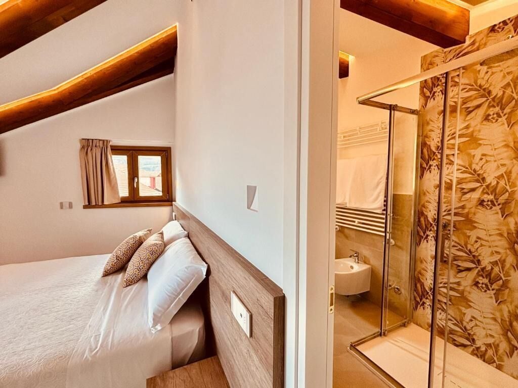 A bedroom with a bed, a window, and a shower area with a glass door.
