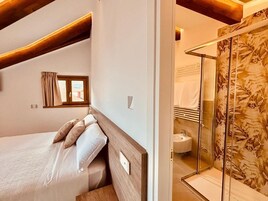 A bedroom with a bed, a window, and a shower area with a glass door.