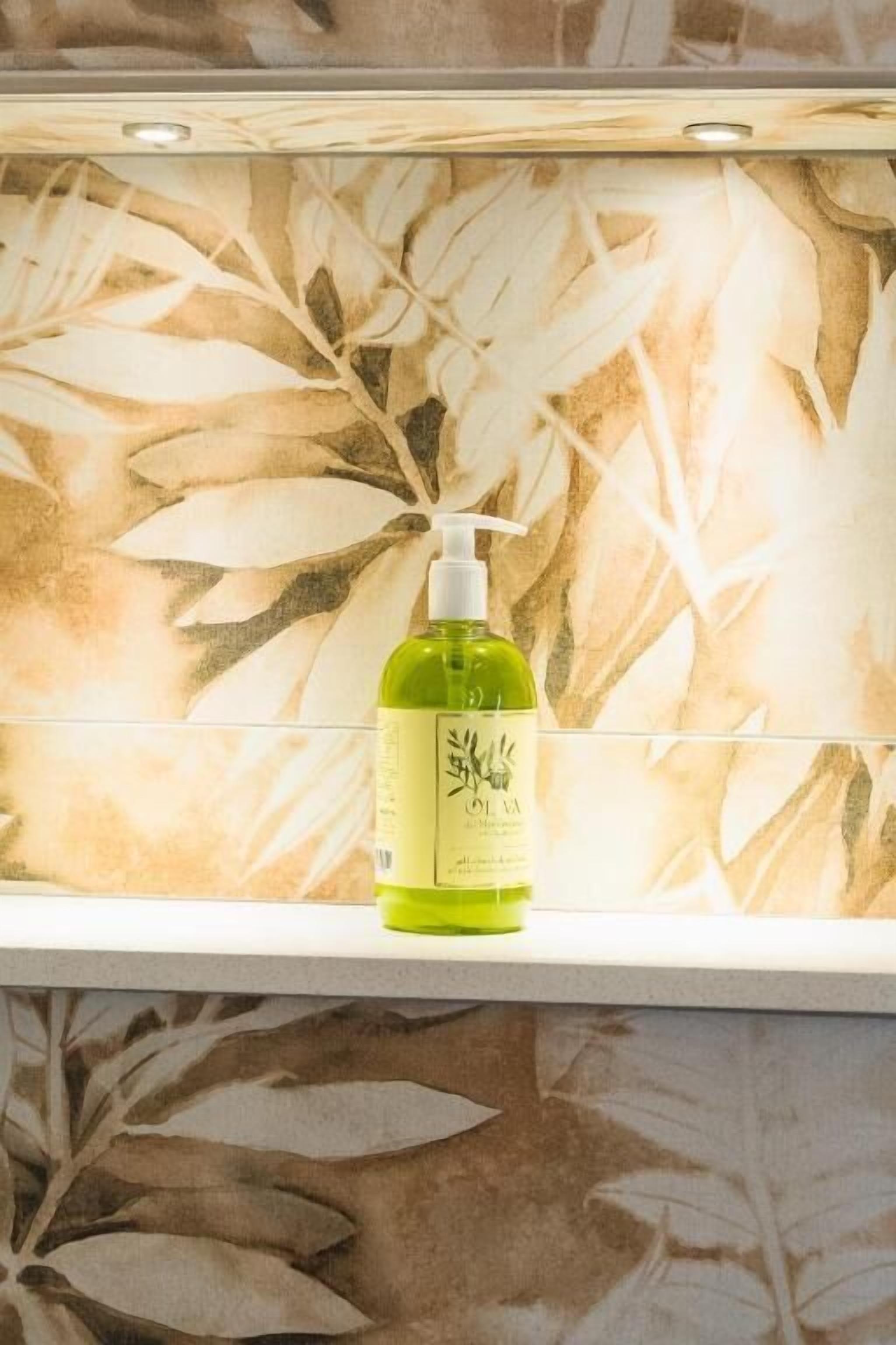 Een fles groene vloeibare zeep op een witte plank voor een muur met een bladmotief.