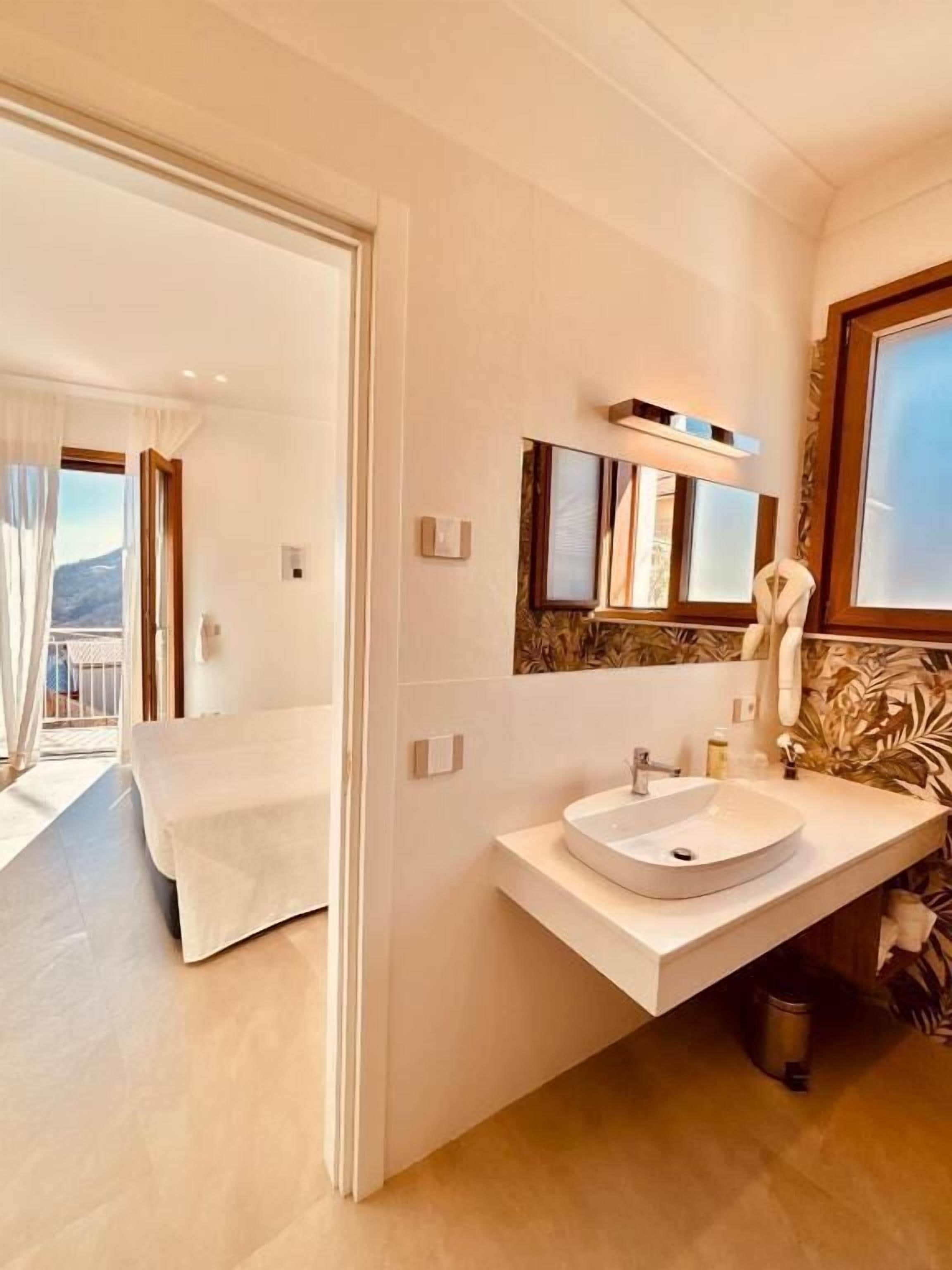 Een moderne badkamer met een grote spiegel, een rond wastafelmeubel en uitzicht op een balkon.