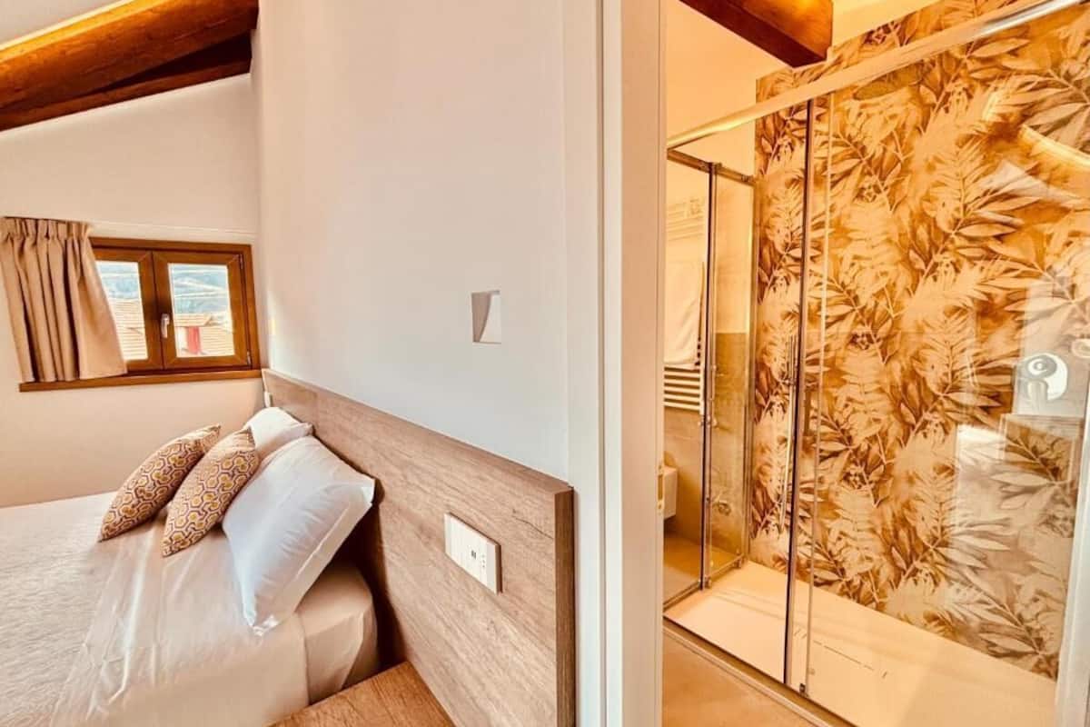 Ein Schlafzimmer mit einem Bett, einem Fenster und einer Dusche mit einem Duschvorhang mit Blättermotiv.