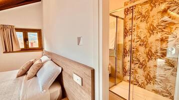 A bedroom with a bed, a window, and a shower with a leaf-patterned shower curtain.