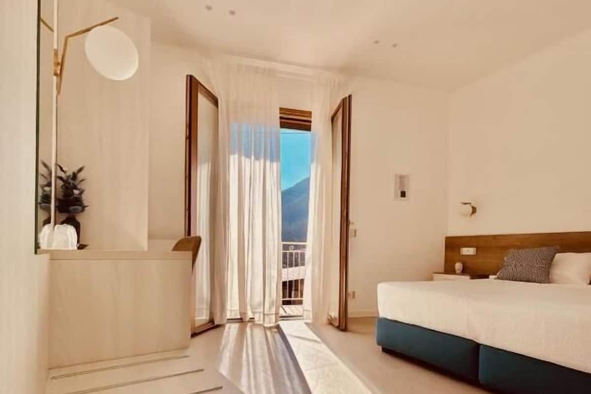 Ein Hotelzimmer mit einer geschwungenen Treppe, einem Bett mit blauen Akzenten, Blick durch ein Fenster und einer Tür zu einem Außenbereich.