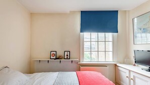 A bedroom with a bed, a window with a view, a shelf with pictures, and a TV on a cabinet. - Room-double Bedroom With own Bathroom in (London)