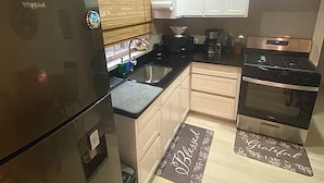 A compact kitchen with a refrigerator, stove, sink, and white cabinets. - Jaden's Guest House - by Zenbreak (Cane Garden)