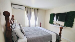 A bedroom with a bed, curtains, a TV, and a small shelf. - Jaden's Guest House - by Zenbreak (Cane Garden)
