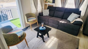 A living room with a sofa, a chair, a small table, and a view through a glass door to an outdoor area. - Jaden's Guest House - by Zenbreak (Cane Garden)