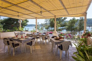 Eine Terrasse im Freien mit Tischen und Stühlen, mit Blick auf ein Gewässer und Hügel.