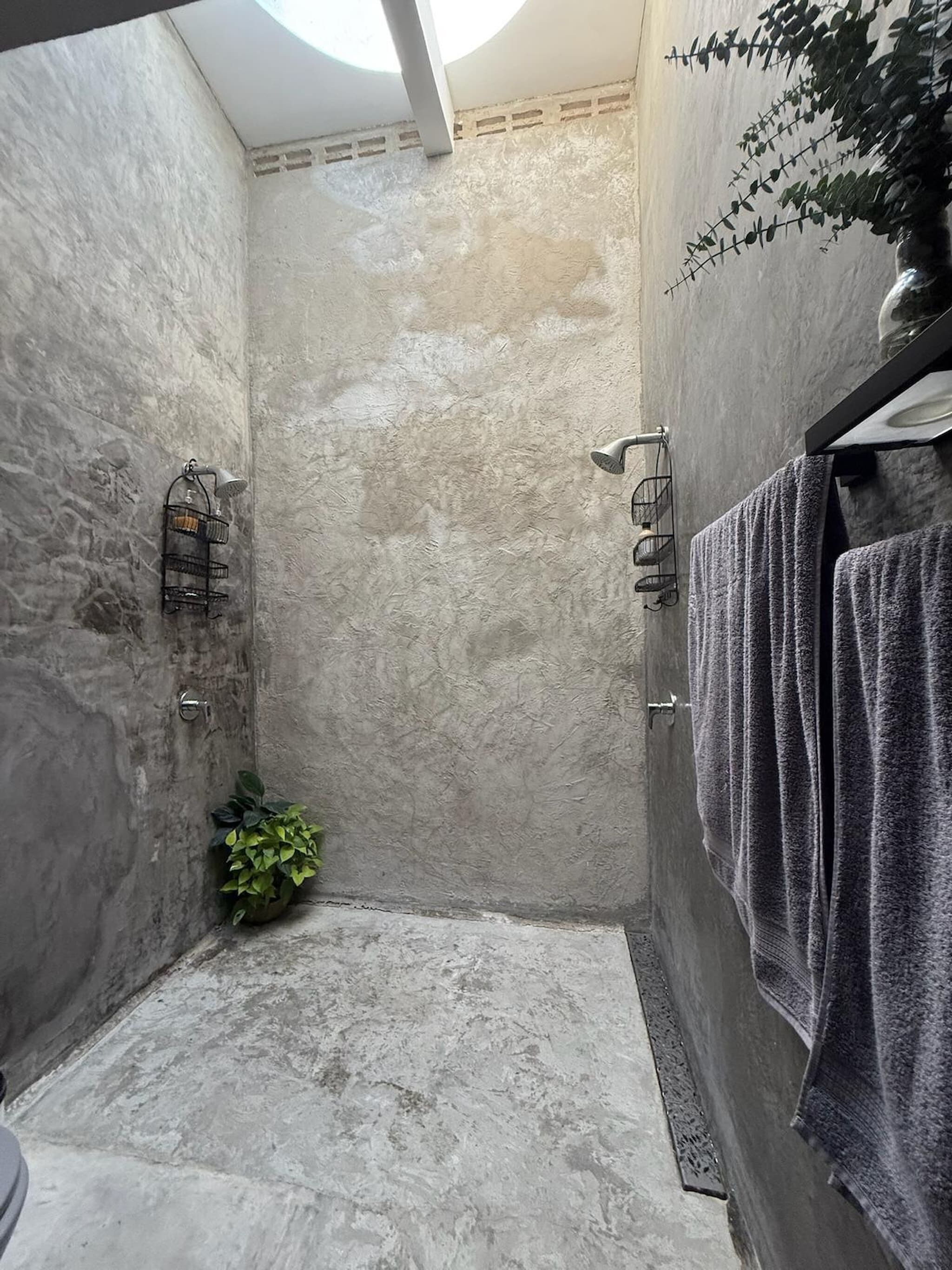 A shower area with a textured wall, a potted plant, and towels.
