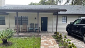 A house with a covered porch, a car parked in the driveway, and a small garden area.