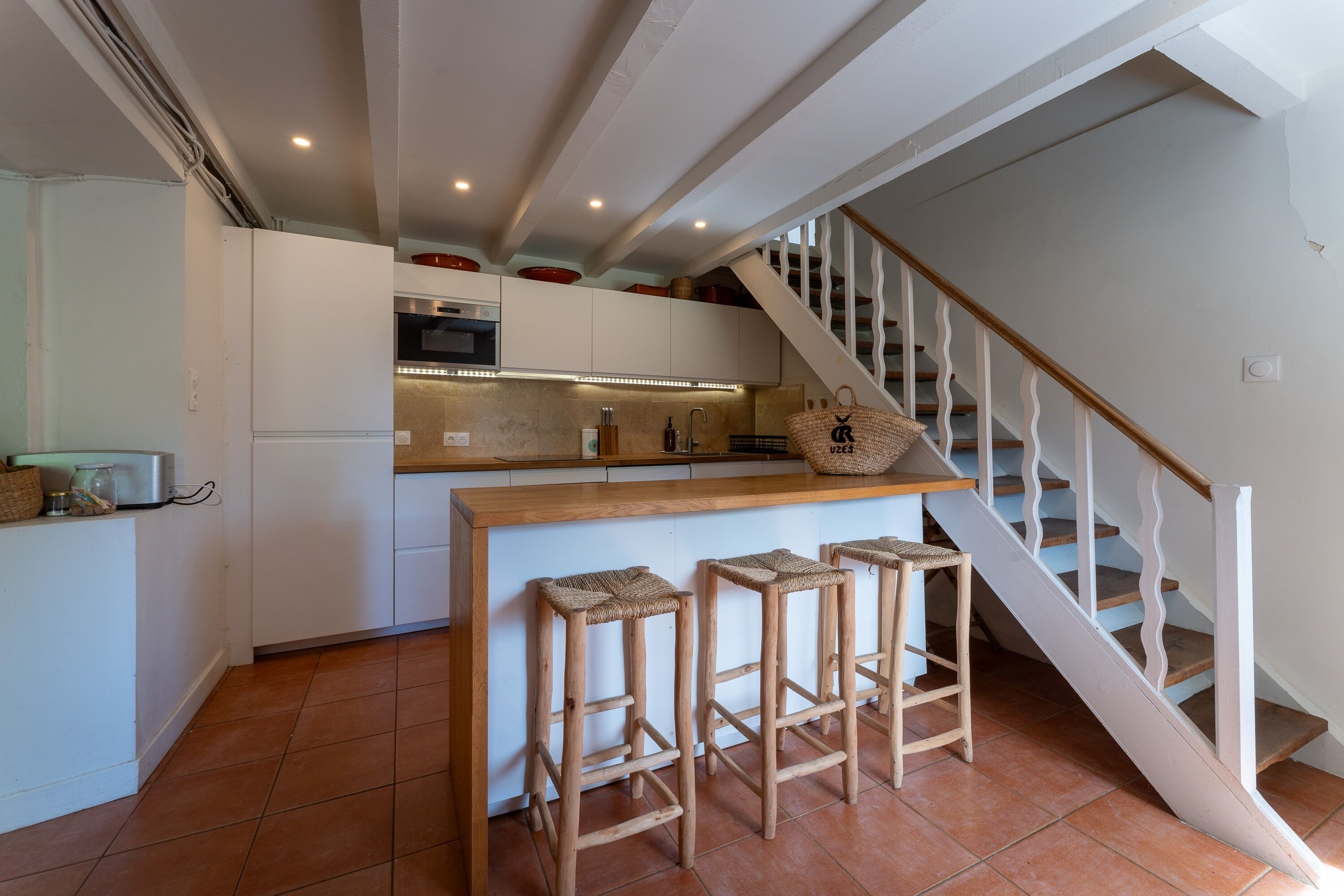 Eine Küche mit einer Holzeinsele, Hockern, einer Treppe und einer Kücheninsel mit Mikrowelle und Backofen.