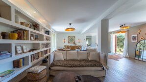 Ein großzügiges Wohnzimmer mit Sofa, zwei kleinen Tischen, einem Bücherregal und einem Essbereich mit Tisch und Stühlen.