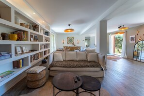A spacious living room with a sofa, two small tables, a bookshelf, and a dining area with a table and chairs. - Grand'maison - Avec piscine privée (Bouquet)