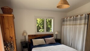 Un dormitori amb un llit, una finestra, una taula de nit, una làmpada, un armari de fusta i un ramó decoratiu.