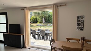Habitació amb televisió sobre un moble de fusta, taula de menjador amb caires, sofà i vista a un pati exterior amb caires i ombrelles.