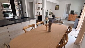 Una cuina moderna amb electrodomèstics integrats, una zona de menjador amb taula i cadires de fusta, i un saló amb sofà i televisió.