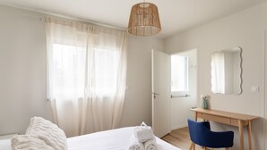 A hotel room with a bed, a desk, a chair, a hanging light fixture, a door, and a mirror. - Casa Fiorenza - À 750 mètres de la plage (Dinard)