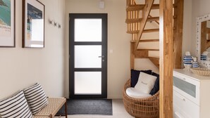 A room with a wooden staircase, a wicker chair, a white dresser, and a black-framed door. - Casa Fiorenza - À 750 mètres de la plage (Dinard)