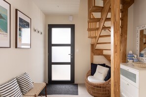 A room with a wooden staircase, a wicker chair, a white dresser, and a black-framed door. - Casa Fiorenza - À 750 mètres de la plage (Dinard)