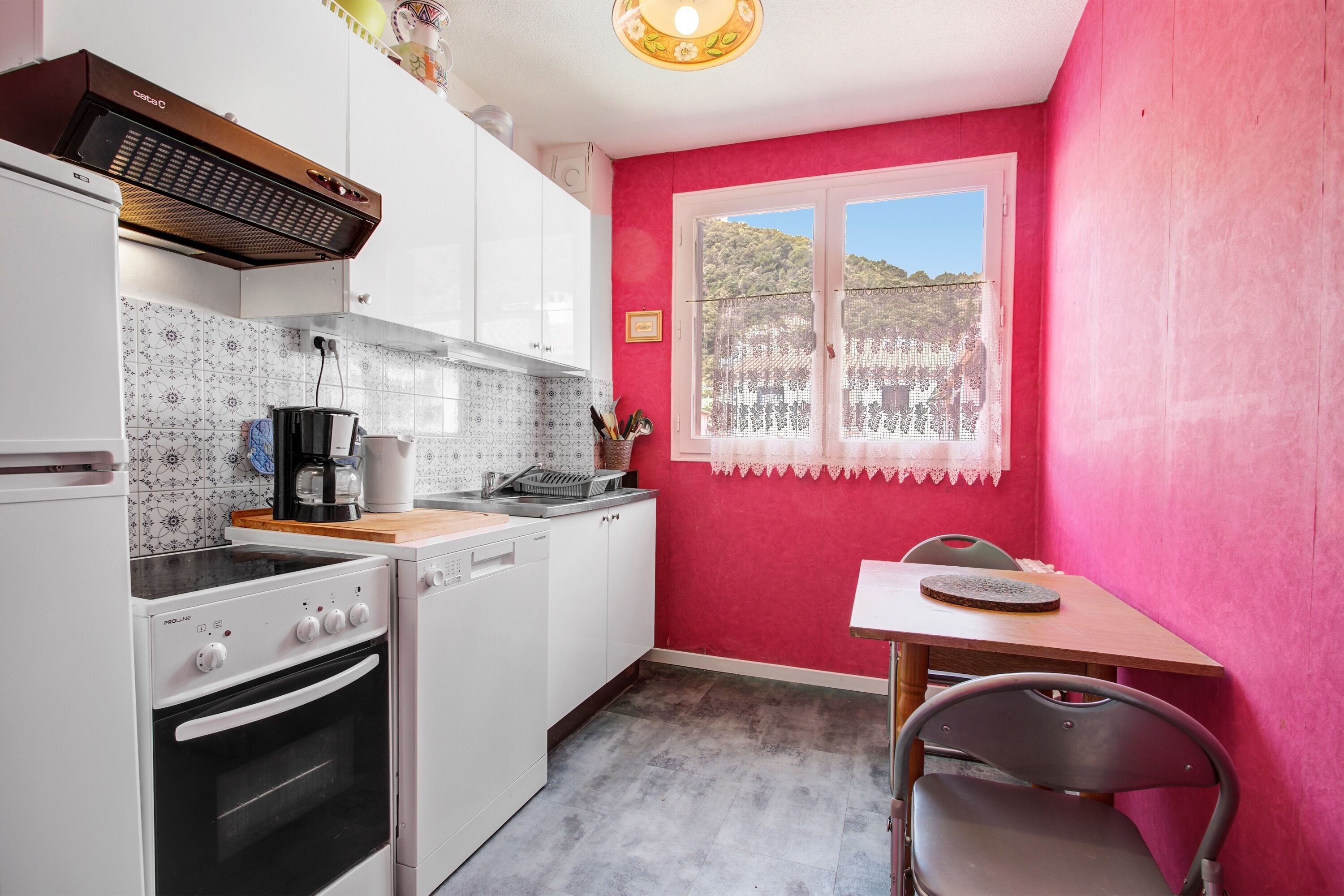 A kitchen with white cabinets, a stove, a coffee maker, and a window with a view of a hill.