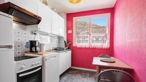 A kitchen with white cabinets, a stove, a coffee maker, and a window with a view of a hill. - L'Écrin Thermal - Appt avec balcon et vue dégagée (Amélie-les-Bains-Palalda)