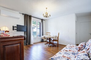 Ein Zimmer mit Holzboden, einem Esstisch mit Stühlen, einer Couch, einem Fernseher und einer Chandelier.