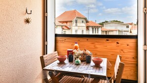 Ein Balkon mit einem Tisch für zwei Personen, eine Holzverkleidung und Blick auf Gebäude mit roten Dächern.
