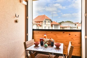 A balcony with a table set for two, a wooden wall, and a view of buildings with red roofs. - Le Clos des Tamaris - Bel appt proche plage (Biscarrosse)