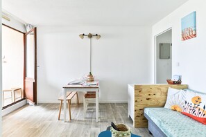 A room with a wooden desk, a chair, a bed with a headboard, a wall-mounted light fixture, and a window with a view. - Le Clos des Tamaris - Bel appt proche plage (Biscarrosse)