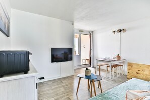 Una habitación con una cama, un televisor, una mesita con sillas, un cabecero de madera y una puerta que da a otra habitación.