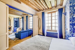 A room with a bed, a blue sofa, a chair, a radiator, and a window with curtains. - Authentic Apartment 1br/3p - Notre Dame (Paris)